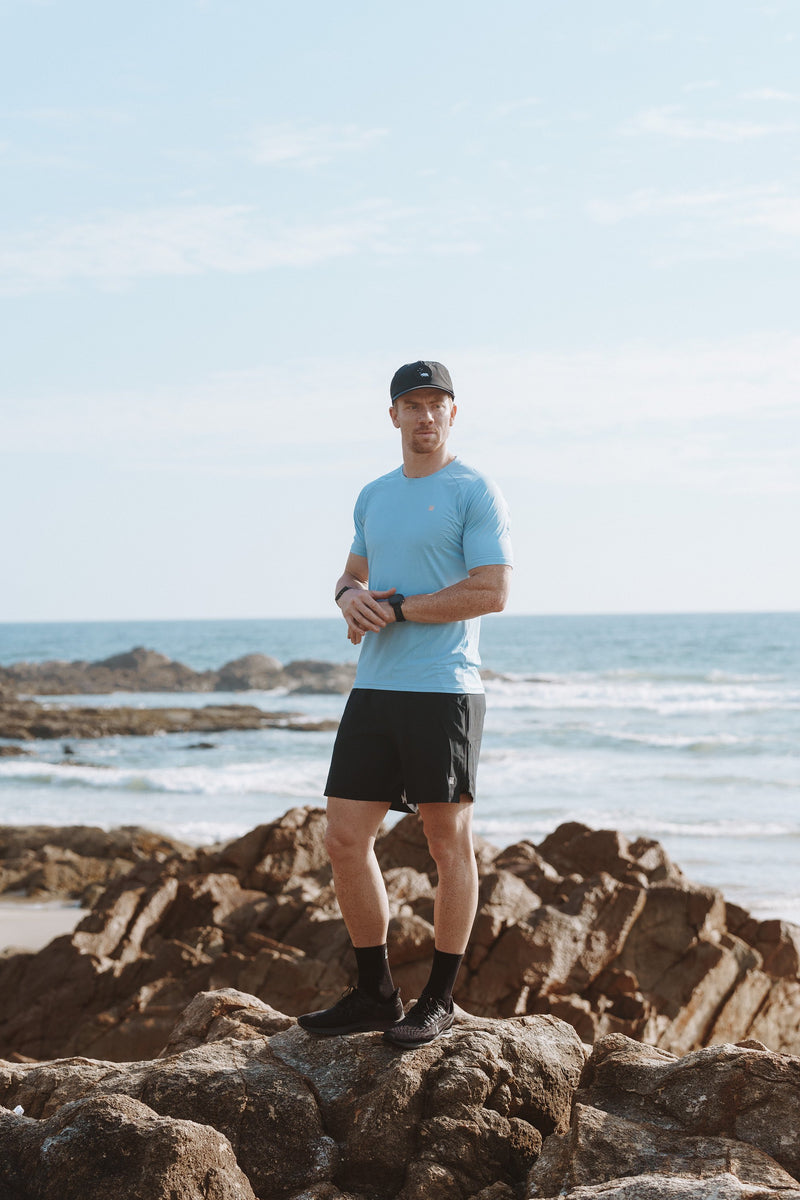 Model wearing black Rep Shorts by the ocean. Men's black athleisure shorts.
