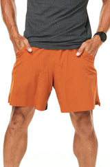 Model with his hands in the pockets of rust Rep Shorts. Men's gym shorts that double as casual wear.