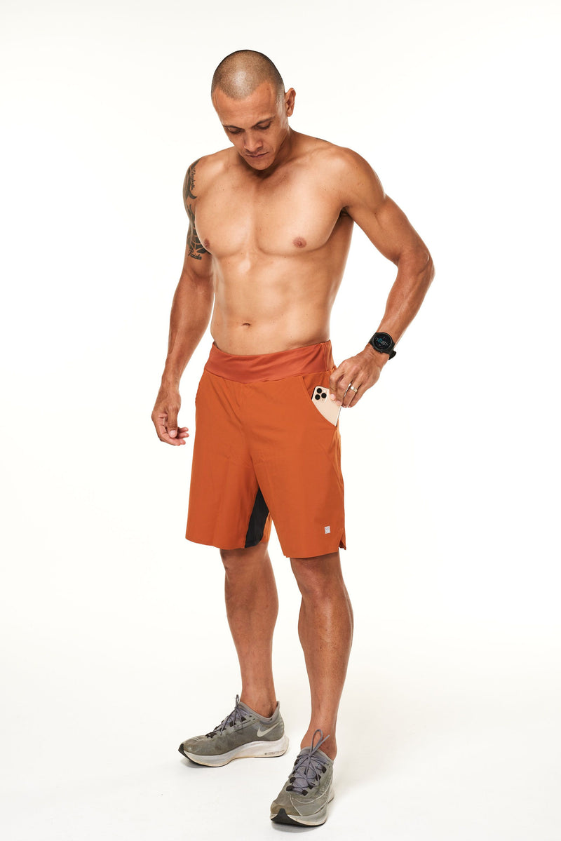 Model placing a phone in the side pocket of his rust Arvo Shorts. Men's gym shorts with pockets.
